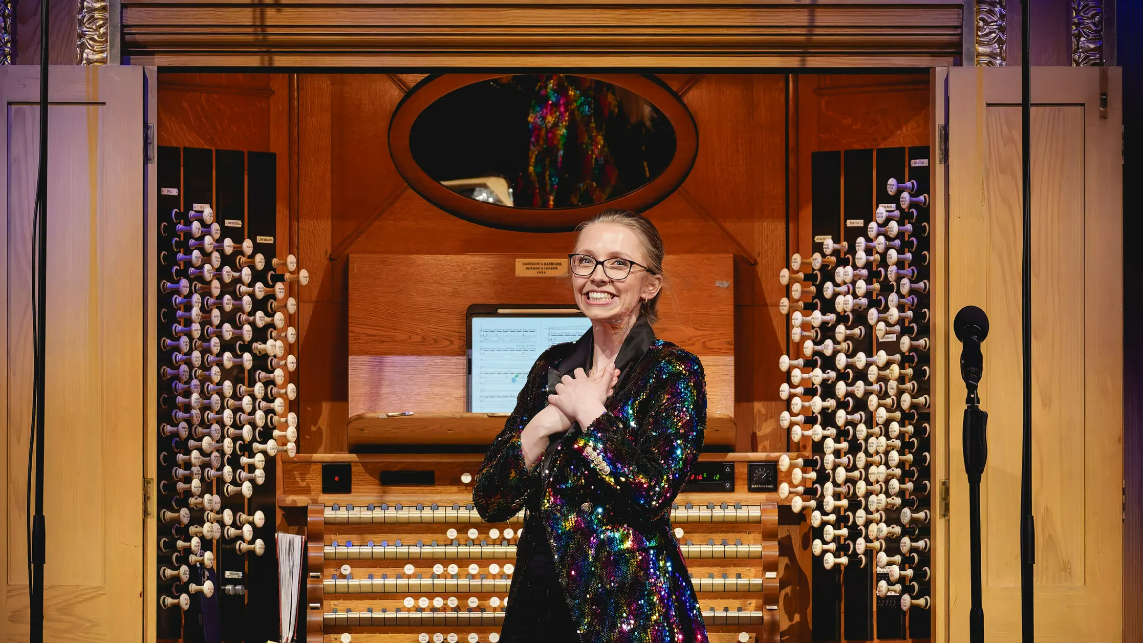 A woman in a sequined jacket standing in front of a pipe organ.